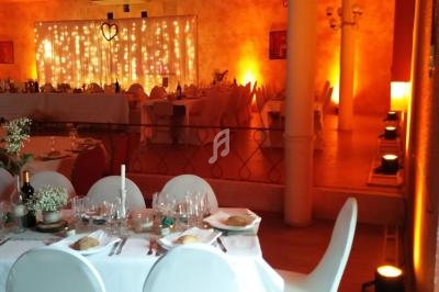 Salle de réception décorée avec des guirlandes lumineuses, tables dressées et éclairage chaleureux.