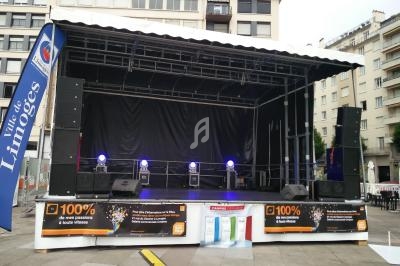 Scène extérieure équipée de projecteurs, installée sur une place urbaine entourée de bâtiments modernes.