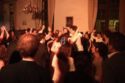 Groupe de personnes dansant dans une salle éclairée de manière tamisée avec des chandeliers et de grandes fenêtres.