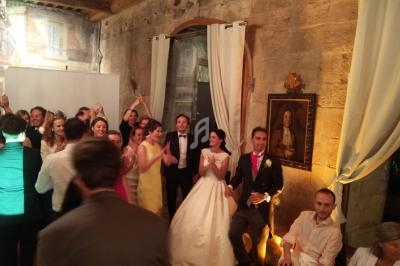 Groupe de personnes dans une salle en pierre, célébrant un mariage avec les mariés au centre en tenue de cérémonie.