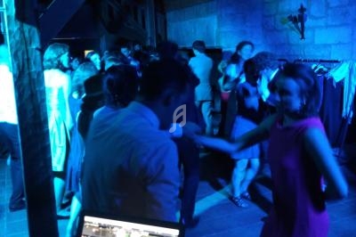 Personnes dansant dans une salle éclairée par des lumières bleues, avec un ordinateur de DJ au premier plan.