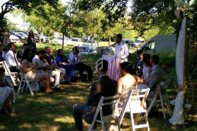 Cérémonie de mariage en plein air avec un officiant s'adressant aux invités assis sous des arbres.