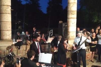 Un groupe de musiciens et une chanteuse se produisent en plein air devant un public, sous un ciel nocturne.
