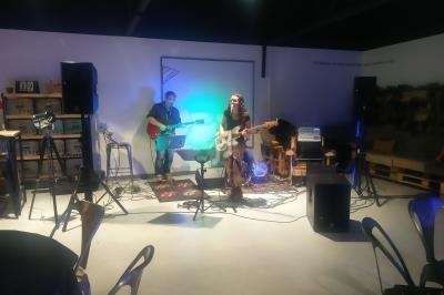 Deux musiciens jouent de la guitare sur une petite scène éclairée dans une salle avec des chaises et du matériel audio.