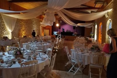 Salle de réception décorée pour un mariage, avec tables dressées, chaises blanches et éclairage chaleureux.