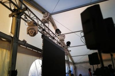 Structure métallique avec projecteurs et écran suspendu dans une tente lumineuse, utilisée pour un événement.
