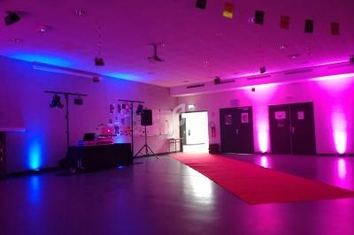 Salle décorée avec éclairages colorés, tapis rouge au sol et matériel de sonorisation installé près d'un mur.