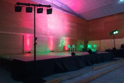 Scène vide dans une salle avec éclairage coloré rose et vert, chaises blanches en arrière-plan.