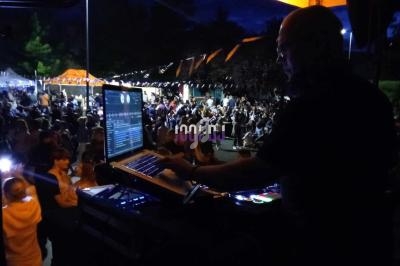 Un DJ mixe sur une scène en plein air, face à une foule rassemblée lors d'un événement nocturne.