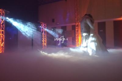 Un couple danse dans une salle éclairée par des projecteurs colorés et entourée de fumée au sol.