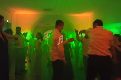 Personnes dansant dans une salle faiblement éclairée avec des lumières vertes et oranges créant une ambiance festive.