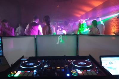 Vue d'une console de DJ en premier plan, avec une piste de danse animée et éclairages colorés en arrière-plan.