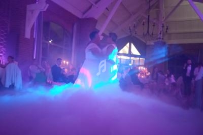 Deux personnes dansent ensemble dans une salle éclairée de lumières colorées, entourées de fumée et d'invités assis.