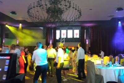 Des personnes dansent dans une salle de réception éclairée par des lumières colorées, avec des tables dressées en arrière…