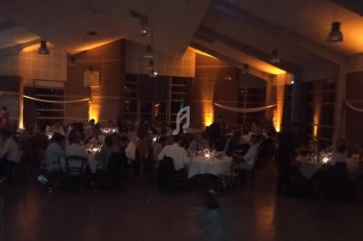 Salle de réception éclairée avec des guirlandes lumineuses, tables dressées et invités assis lors d'un événement en soirée.