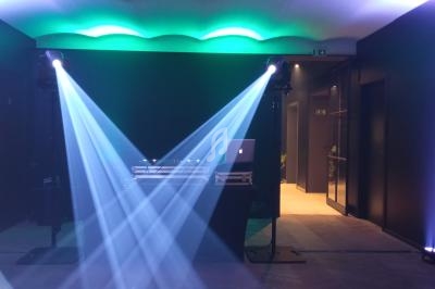 Jeux de lumières bleues et vertes éclairant une salle sombre avec une table de DJ et un ordinateur portable.