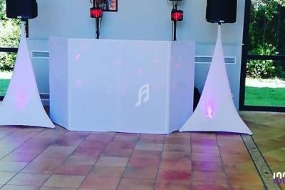 Installation de matériel de sonorisation et éclairage avec une table de DJ recouverte d'un tissu blanc.