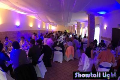 Des convives assis à des tables rondes dans une salle éclairée par des lumières colorées, lors d'un événement festif.