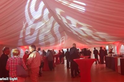Des personnes rassemblées dans une grande tente éclairée de lumières rouges, avec des tables hautes et un buffet.