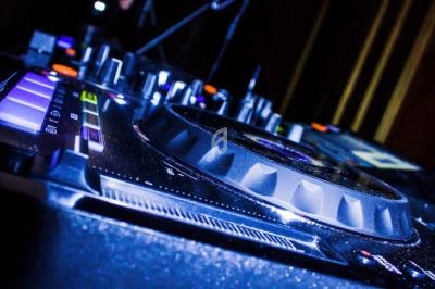 Main posées sur un contrôleur DJ Pioneer avec un ordinateur portable en arrière-plan dans un environnement sombre.