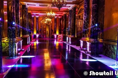 Salle de réception luxueuse avec colonnes en marbre, éclairages colorés et lustres suspendus.