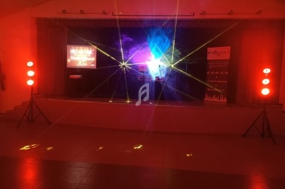 Scène éclairée par des projecteurs rouges et des faisceaux lumineux, avec des écrans et rideaux en arrière-plan.