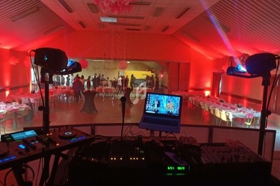 Salle de réception éclairée en rouge avec tables dressées, vue depuis une régie DJ équipée d'ordinateurs et de consoles.