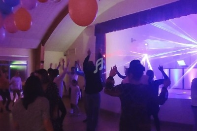 Des personnes dansent dans une salle éclairée par des lumières colorées et des lasers, avec des ballons suspendus au plafond.