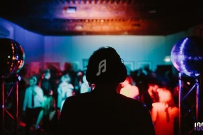 Une silhouette de DJ devant une foule dans une salle éclairée par des lumières colorées et des boules à facettes.