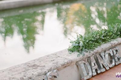 Lettres lumineuses formant le mot ’DANCE’ posées près d'un bassin entouré de végétation.