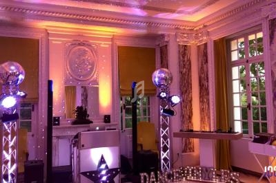 Salle élégante avec décor lumineux, boules à facettes et équipement de DJ installé devant des fenêtres ouvertes.