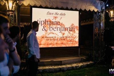 Écran affichant une invitation de mariage avec des prénoms, une date et un lieu, sous un éclairage extérieur nocturne.