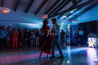 Un couple danse sur une piste éclairée par des lumières colorées, entouré d'invités qui les regardent.