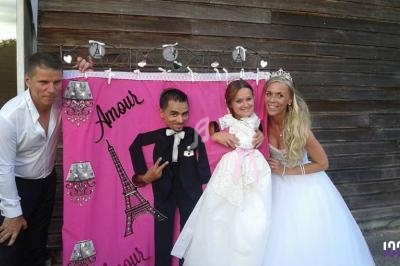 Quatre personnes posent devant un décor rose avec des motifs de mariage et de la Tour Eiffel.