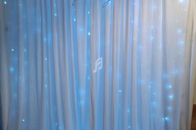 Rideau blanc illuminé par des guirlandes lumineuses bleues, avec des initiales décoratives en haut.