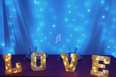Lettres lumineuses formant le mot ’LOVE’ posées sur une table rouge, avec un fond de guirlandes lumineuses bleues.