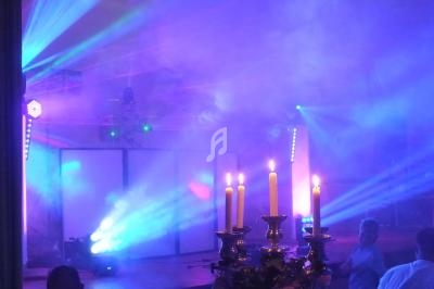 Salle de fête éclairée par des lumières colorées, avec un chandelier au premier plan et des effets de fumée.