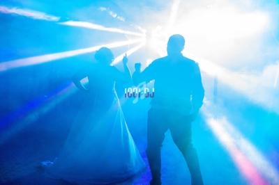 Un couple danse sous des lumières colorées et des effets de fumée dans une ambiance festive.