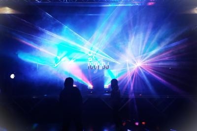 Deux personnes dansent devant une scène illuminée par des jeux de lumières colorés et des faisceaux laser.