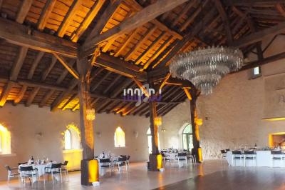 Salle de réception avec charpente en bois apparente, lustre imposant et tables dressées pour un événement.