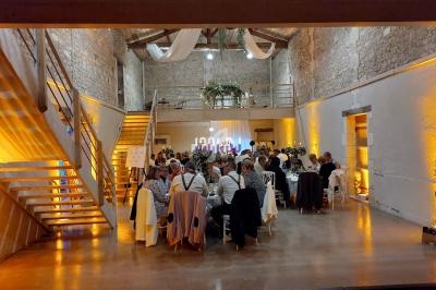 Salle en pierre avec des invités assis à des tables rondes pour un dîner, éclairage chaleureux et décorations suspendues.