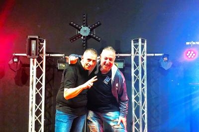 Deux hommes souriants posent devant une installation lumineuse avec projecteurs colorés en arrière-plan.