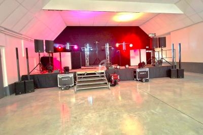 Scène équipée de matériel audio et éclairage coloré dans une salle vide au sol en béton.