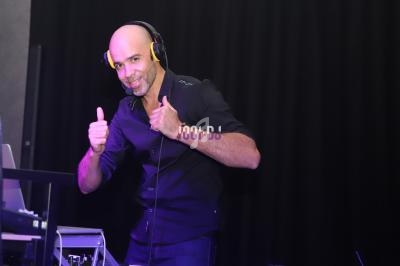 Un DJ souriant portant un casque audio fait un geste de pouce levé devant son équipement, sur fond sombre.