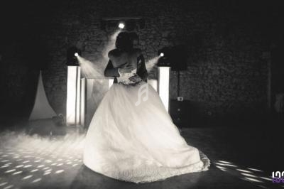 Un couple danse enlacé sous des lumières tamisées dans une salle en pierre, créant une ambiance romantique.