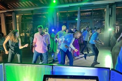 Des personnes dansent sous des lumières colorées dans une salle avec de grandes baies vitrées en arrière-plan.