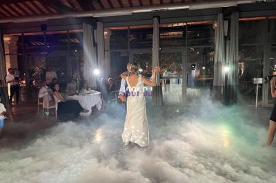 Une femme en robe blanche danse dans une salle éclairée, entourée de fumée et de spectateurs assis.