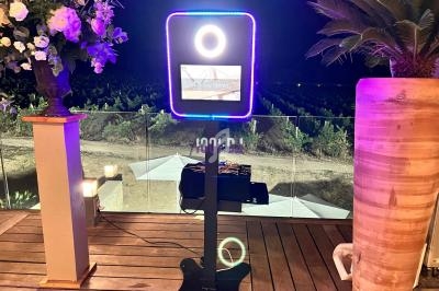 Borne photo lumineuse sur une terrasse en bois, avec vue nocturne sur un paysage extérieur et des plantes décoratives.