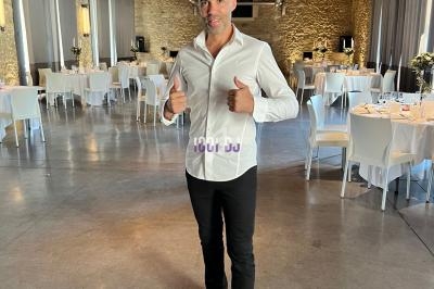 Homme debout dans une salle de réception lumineuse avec tables dressées, donnant deux pouces levés.