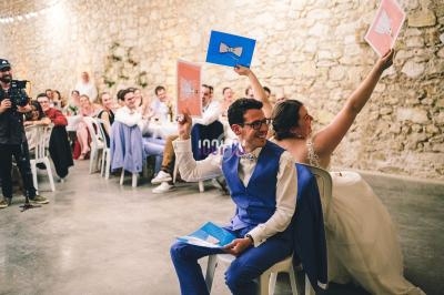 Un couple joue à un jeu lors d'une réception de mariage, assis dos à dos et levant des panneaux colorés.